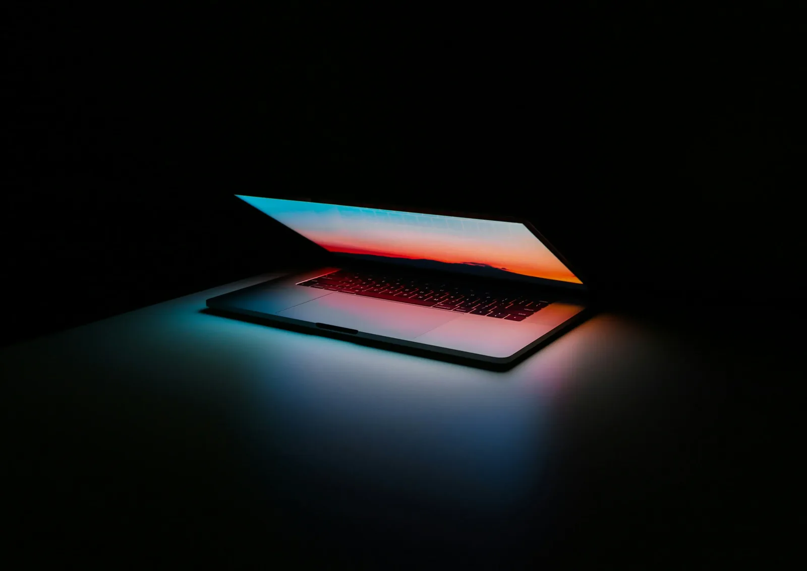 A laptop open on a desk in a dark room, used to manage cloud-based digital signage screens remotely.