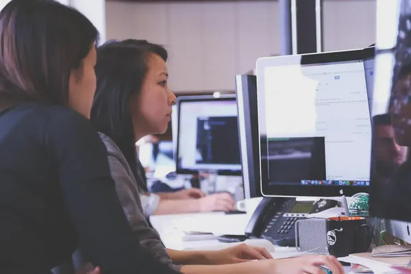 Two women at a desktop computer learning about digital signage cloud software options.