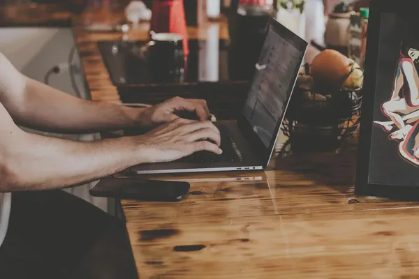 A man at a wooden desk choosing a digital signage platform using his laptop.