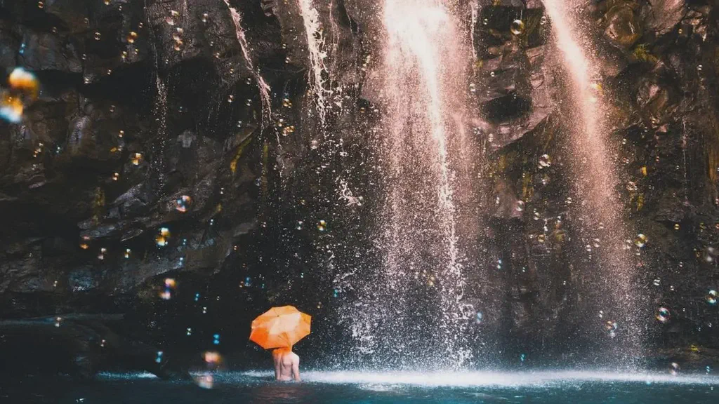 This is an image from Unsplash for use with digital signage of man under a waterfall with an orange umbrella.