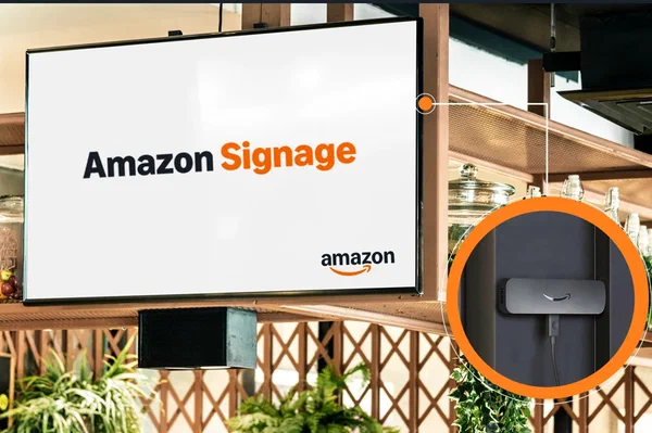 Amazon Signage Stick plugged into a wall-mounted screen displaying the Amazon Signage logo